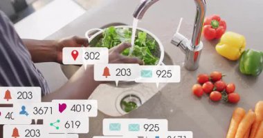 Adam mutfakta yapraklı yeşillikleri musluk altında yıkıyor, yemek blogları için sosyal medya ölçüleri gösteriyor. Taze ürünler, mutfak gereçleri, dijital bağlılık, sağlıklı beslenme, ev ortamları, canlı renkler, mutfak aktiviteleri