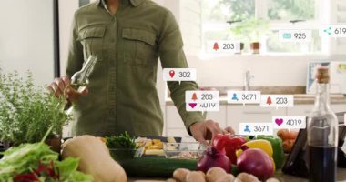 Kadın mutfağa yağ döküyor, aşçılık dersleri veriyor, yüzen sosyal medya simgeleriyle. Taze üretim, aşçılık, dijital bağlılık, modern mutfak, sağlıklı yaşam tarzı, sosyal medya, yaşam tarzı içeriği