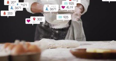 Yetişkin bir erkek fırıncı fırında hamurun üzerinde süzgeçle un seçiyor ve nişan ikonları sergiliyor. Pişirme, aşçılık, profesyonellik, zanaat, mutfak, zanaat, gastronomi.