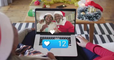 Aile üyeleri oturma odasında teknolojik tatillere katılıyorlar. Animasyon kar taneleri ve hediye ikonlarıyla. Şenlik, teknoloji, kutlama, sıcaklık, gelenek, bağlantı, konforlu