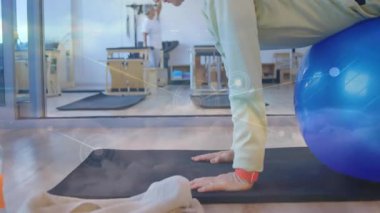 Pilates stüdyosunda mavi denge topuna yaslanan yaşlı bir kadın animasyon istatistikleri gösteriyor. Fitness, sağlık, güç, esneklik, gençleşme, ergonomik, aktif yaşlanma