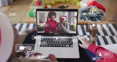 Oturma odasında dizüstü bilgisayarla oturan kullanıcı anne ve kızını arıyor, sosyal medya simgelerini gösteriyor. Şenlik, tatil, bağlantı, kutlama, sıcaklık, dijital, aile