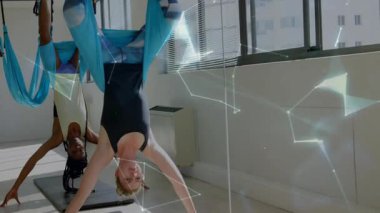 İki kadın yoga stüdyosunda mavi hamakla baş aşağı poz vererek dijital sağlık örtüsü gösteriyorlar. Zindelik, sağlık, esneklik, farkındalık, dinginlik, çağdaş, bütünsel