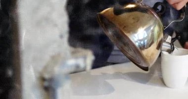 Çelik çaydanlıktan kupaya sıcak su döken adam, noktalı kaplamalarla gıda endüstrisini vurguluyor. Yansıtıcı, minimalizm, rahat, paslanmaz, içecek, yerli, modern