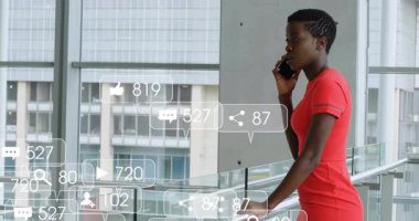 Teknoloji salonunda cam korkuluklara yaslanan, akıllı telefon kullanan, sosyal simgeleri havada uçuşan bir kadın. Kentsel, kurumsal, iletişim, yenilik, gösterişli, profesyonel, bağlantı