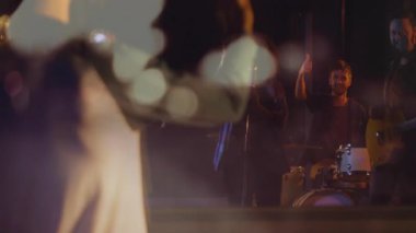 Grup arkadaşları sahne ışıkları altında konser veriyor, kulaklıklar, mikrofon, davul setleri üzerinde animasyon notaları gösteriyorlar. Müzisyenler, performans, heyecan, ritim, eğlence, sahne, profesyonel