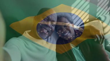 Olgun bir çift, teknoloji reklamı için Brezilya bayrağını gösteren akıllı telefon kullanarak kanepeye yaslanıyor. Şefkat, samimiyet, bağlantı, sıcaklık, emekli, rahat, yaşam tarzı