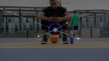 Topun üzerine çömelmiş bir adam açık hava spor sahasında akıllı telefonu tutuyor, veri ağı örtüsünü gösteriyor. Atletik, takım çalışması, yenilik, dijital, modern, fitness, teknoloji