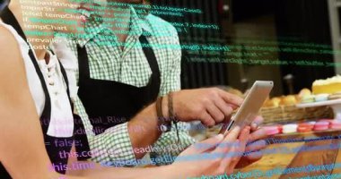 Baristas, Hasır pasta sepetinin yanındaki akıllı telefonu kontrol ederken gülüyor ve üzerinde teknoloji kodu var. Fırın, takım çalışması, modern, dijital, konukseverlik, neşeli, sıradan