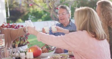 Video of happy caucasian parents, daughter and grandparents making a toast at outdoor dinner table. Family, domestic life and togetherness concept digitally generated video.