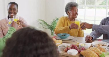 Afro-Amerikan ebeveynlerin, kız ve büyükbabaların yemek masasında kadeh kaldırışlarının videosu. Aile, aile hayatı ve birliktelik kavramı dijital olarak oluşturulmuş video.