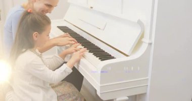 Müzik öğretmeni piyano tuşlarında kızların parmaklarına rehberlik ediyor, ellerini yerleştiriyor ve notalar havada süzülürken salınıyor. Piyano, akıl hocalığı, eğitim, uyum, ilham, minimalist, yerli