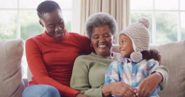 Afro-Amerikan anne, kız ve büyükannenin kanepede oturup kucaklaştığı gülümseme videosu. Aile, aile hayatı ve birliktelik kavramı dijital olarak oluşturulmuş video.