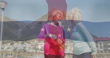 Şişenin kapağını açan orta yaşlı bir kadın hidrasyon ikonlarıyla korkuluklardan aşağı iniyor. Açık hava, dostluk, refah, boş zaman, sahil, manzara, canlı