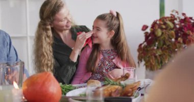 Video of happy caucasian mother cleaning daughter's face at family dinner table. Family, domestic life and togetherness concept digitally generated video.