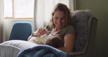 Yeni doğmuş bebeği koltukta besleyen mutlu beyaz bir annenin videosu. annelik, ebeveyn sevgisi ve yeni doğan bebek konseptiyle ilgilenmek dijital olarak üretilmiş video.