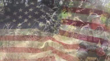 Bayrağın belirdiği yerde, askeri eğitim için çömelmiş ağaçları tarayan bir asker. Vatanseverlik, dayanıklılık, kamuflaj, ihtiyat, açık hava, taktik, yiğitlik