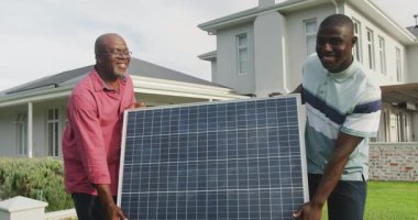 Güneş panelini taşıyan iki Afrikalı Amerikalı adamın videosu. Enerji, enerji ve yakıt teknolojisi ve dijital arayüz konsepti dijital olarak oluşturulmuş video.