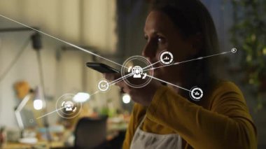 Akıllı telefona konuşan bir kadın, sesli komut kullanarak ağ büyümesini görselleştiren teknik simgeleri etkinleştiriyor. Teknoloji, bağlantı, yenilik, dijital, otomasyon, akıllı, ağ