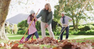 Video of happy caucasian grandparents and granddaughter raking up autumn leaves in sunny garden. Family, domestic life and togetherness concept digitally generated video.