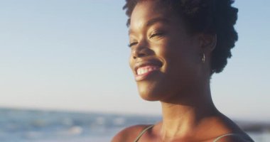 Video of african american woman standing on beach at sunset. Holidays, vacations, relax and spending quality time on beach.