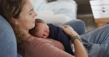 Yeni doğmuş bir bebekle koltukta uyuyan yorgun beyaz annenin videosu. annelik, ebeveyn sevgisi ve yeni doğan bebek konseptiyle ilgilenmek dijital olarak üretilmiş video.