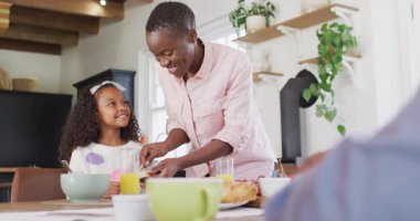Afrika kökenli mutlu bir Amerikalı annenin aile kahvaltı masasında kızına tereyağlı ekmek yediği bir video. Aile, aile hayatı ve birliktelik kavramı dijital olarak oluşturulmuş video.