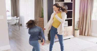 Mutlu Asyalı anne ve kızının oturma odasında dans edişinin videosu. Aile, annelik, ilişkiler ve birlikte kaliteli zaman geçirme konsepti dijital olarak oluşturulmuş video.