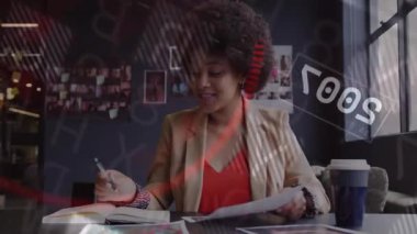 Defter sayfalarını çeviren bir kadın gerçek zamanlı veri örtüşmelerini canlandırıyor ve iş haritalarını analiz ediyor. İş kadını, çalışma alanı, veri görselleştirme, teknoloji, profesyonel, dijital arayüz, analiz