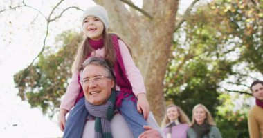Video of happy caucasian grandfather walking with smiling granddaughter on shoulders in sunny garden. Family, domestic life and togetherness concept digitally generated video.