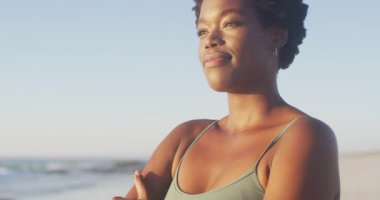 Video of african american woman standing on beach at sunset. Holidays, vacations, relax and spending quality time on beach.