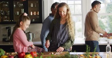 Video of happy caucasian parents and daughter having fun cooking with grandfather in kitchen. Family, domestic life and togetherness concept digitally generated video.