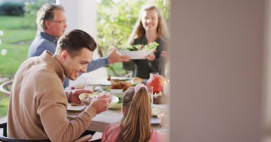 Video of happy caucasian parents, daughter and grandparents serving food at outdoor table. Family, domestic life and togetherness concept digitally generated video.