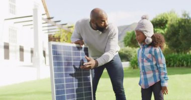 Mutlu Afro-Amerikan babasının güneşli bahçede kızına güneş panelini açıklarken çekilmiş bir video. Aile, aile hayatı ve birliktelik kavramı dijital olarak oluşturulmuş video.