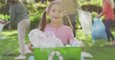 Video portrait of smiling caucasian girl collecting plastic for recycling with family outdoors. Family, domestic life, togetherness, recycling and waste concept digitally generated video.