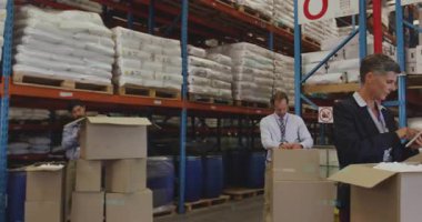 Operatör, takım tableti referans gösterirken lojistik için bant ayırıcı ve karton mühür seçiyor. Depo, lojistik, ambalaj, takım çalışması, sanayi, verimlilik, modern