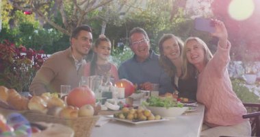 Video of happy caucasian parents, daughter and grandparents taking selfie at outdoor dinner table. Family, domestic life and togetherness concept digitally generated video.