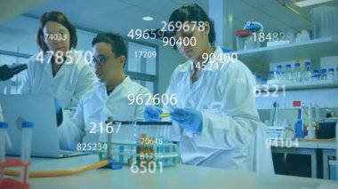 Üç bilim adamı test tüpünü kaldırıyor ve laboratuvar veri analizi için yüzen sayısal ölçümler oluşturuyorlar. Araştırma, yenilik, deney, laboratuvar, bilim, teknoloji, işbirliği