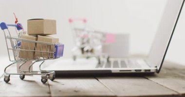Masadaki dizüstü bilgisayarın yanındaki alışveriş arabasındaki kutular. Küresel iş, çevrimiçi alışveriş, siber pazartesi, satış ve perakende konsepti dijital olarak oluşturulmuş video.