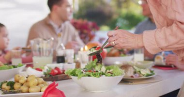 Video of happy caucasian parents, daughter and grandparents serving food at outdoor table. Family, domestic life and togetherness concept digitally generated video.