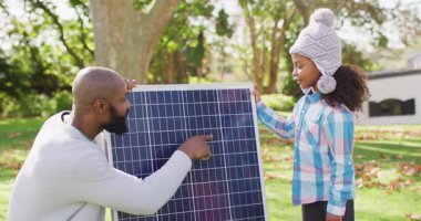 Mutlu Afro-Amerikan babasının sonbahar bahçesinde kızına güneş panelini açıklarken çekilmiş bir video. Aile, aile hayatı ve birliktelik kavramı dijital olarak oluşturulmuş video.