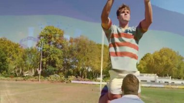 Rugby takım arkadaşları sahada kaldırma sinyali veriyor, ileri kaldırıyor ve bayrak arması ile topu yakalıyorlar. Atletizm, takım çalışması, rekabet, spor, fiziksel, açık hava, zafer