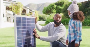 Mutlu Afro-Amerikan babasının güneşli bahçede kızına güneş panelini açıklarken çekilmiş bir video. Aile, aile hayatı ve birliktelik kavramı dijital olarak oluşturulmuş video.