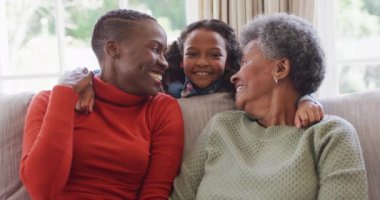 Gülümseyen Afrikalı Amerikalı anne, kız ve büyükannenin oturma odasında otururken videosu. Aile, aile hayatı ve birliktelik kavramı dijital olarak oluşturulmuş video.