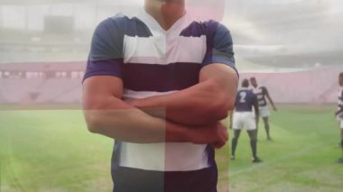 Rugby oyuncusu yumruklarını sıkıyor, maç hazırlığı için kollarını kavuşturuyor, kırmızı haç grafiği sahada kayboluyor. Atletizm, takım çalışması, kararlılık, odaklanma, spor, dayanıklılık, rekabet