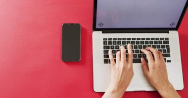 Eller kırmızı masada bilgisayarı ve akıllı telefonu kullanıyor. İş, iletişim ve uzaktan çalışma konsepti dijital olarak oluşturulmuş video.