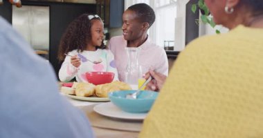 Mutlu Afro-Amerikan kızının aile kahvaltı masasında gülüp annesini beslediği bir video. Aile, aile hayatı ve birliktelik kavramı dijital olarak oluşturulmuş video.