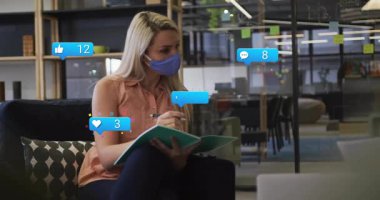 Ofiste notlar yazan bir kadın gazeteyi incelerken sosyal medya simgelerini yükseltmeye başlıyor. İşbirliği, iletişim, modern, ağ oluşturma, üretkenlik, dijital, takım çalışması