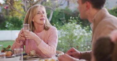 Video of happy caucasian senior mother and adult son talking at outdoor family dinner table. Family, domestic life and togetherness concept digitally generated video.