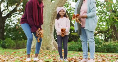 Mutlu Afrikalı Amerikalı anne, kız ve büyükannenin bahçeye sonbahar yaprakları attığı video. Aile, aile hayatı ve birliktelik kavramı dijital olarak oluşturulmuş video.